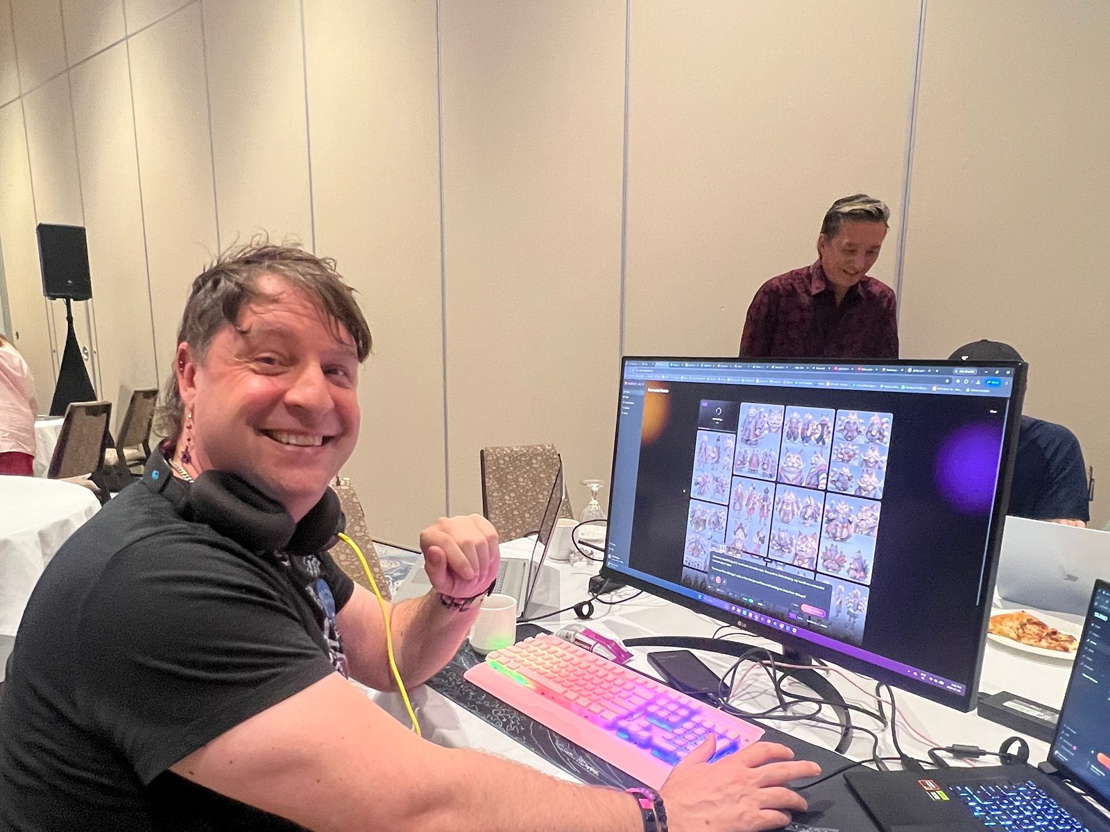 A hack-a-thon participant at his workstation with generated character concepts on screen, with a teammate reviewing footage in the background