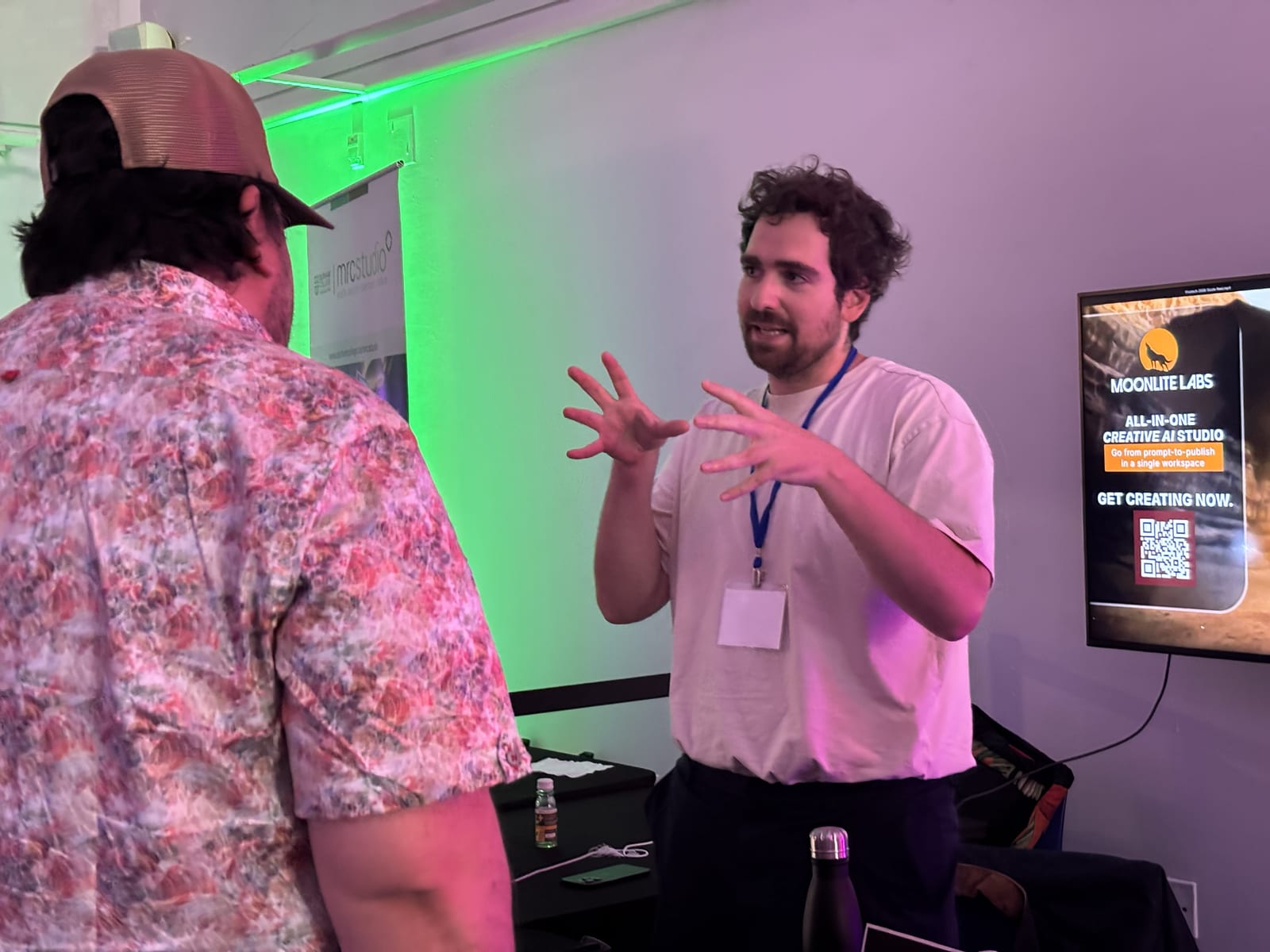 Adam Fainman speaking with an attendee at VRTO 2026 beneath green and pink event lighting, with the Moonlite Labs booth behind them